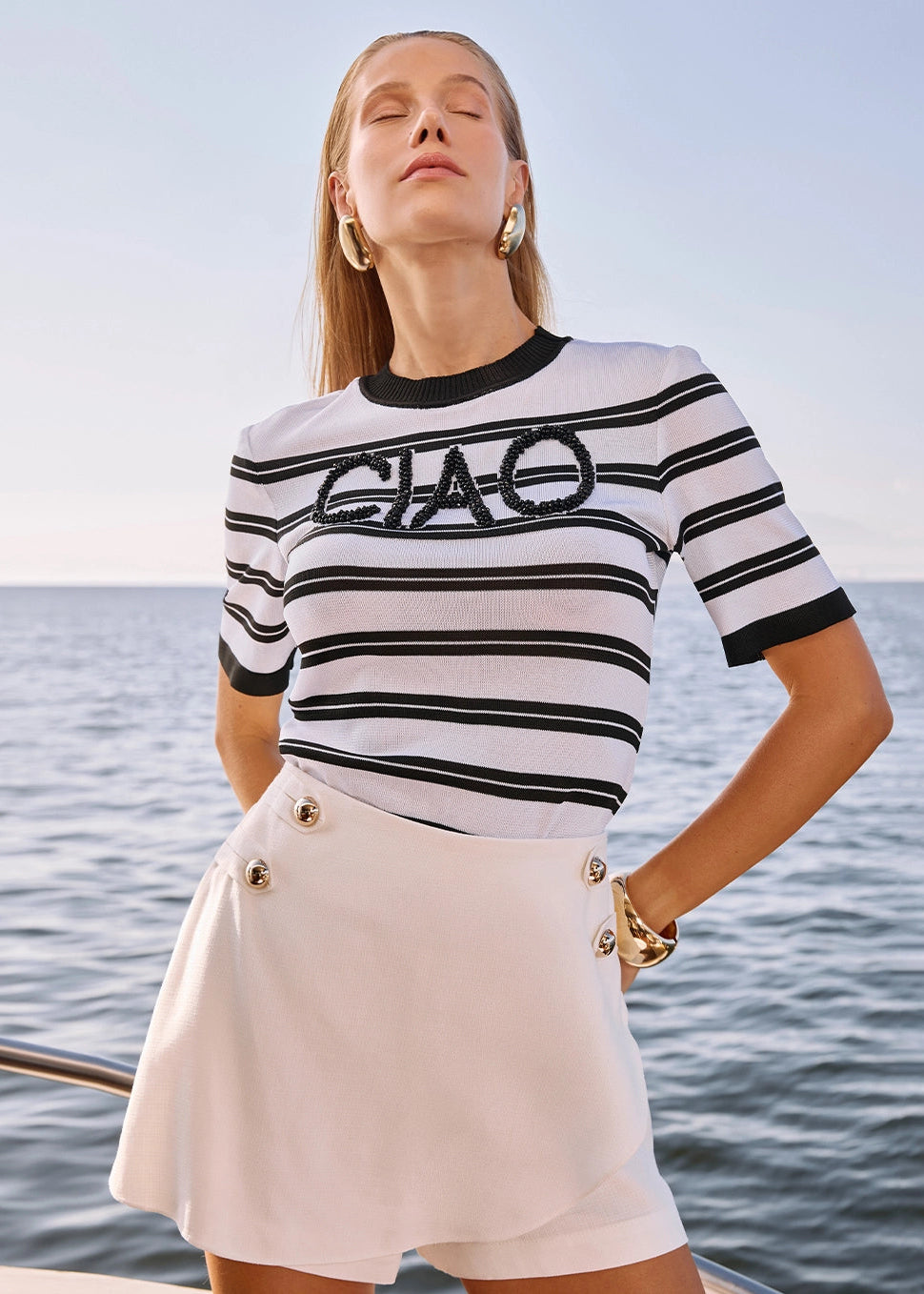 Woman wearing a striped shirt with 'CIAO' text by the water