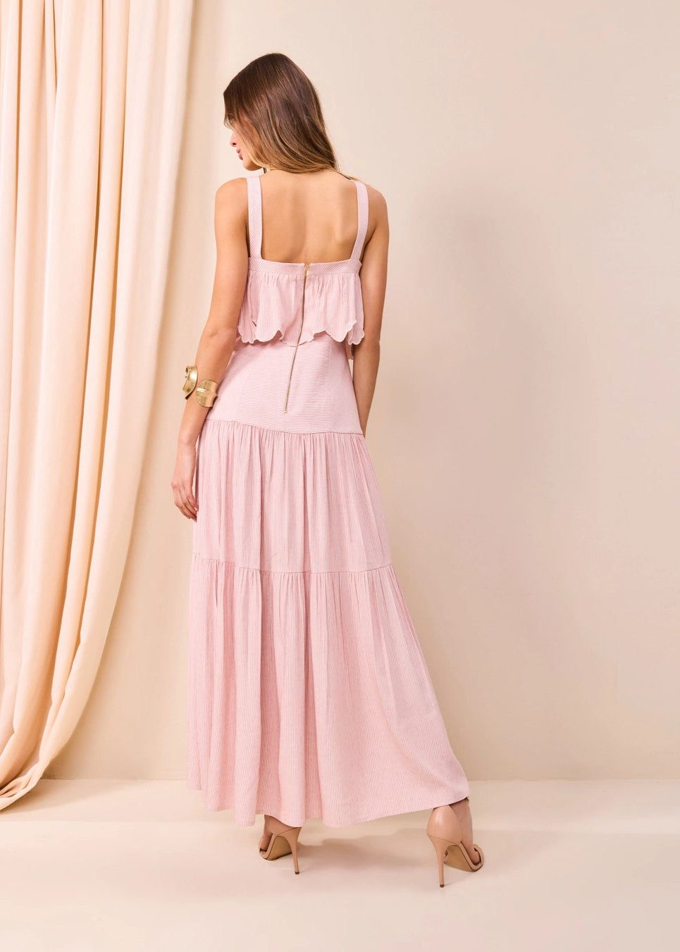 Woman wearing a pink dress standing in front of a beige curtain.