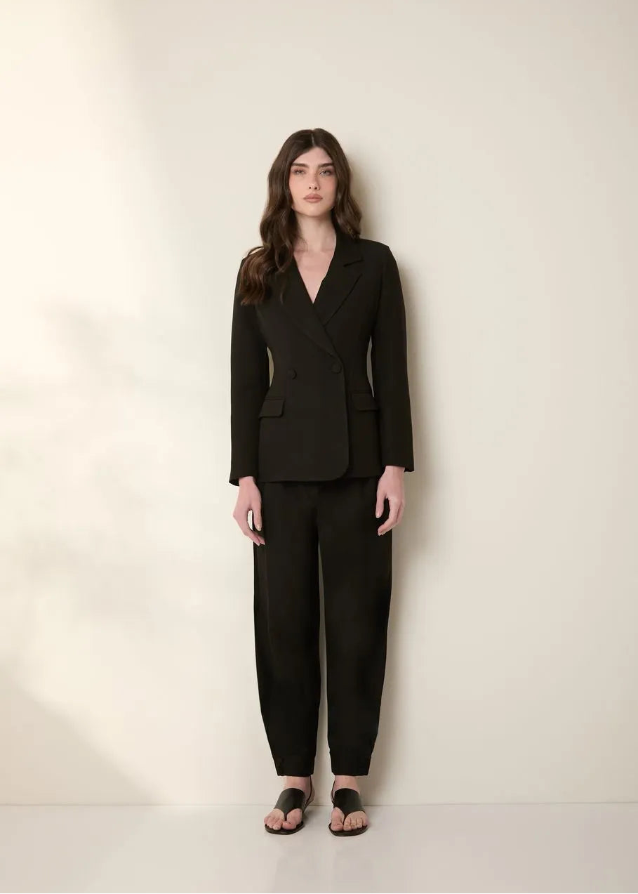 Woman wearing a black suit standing against a plain background