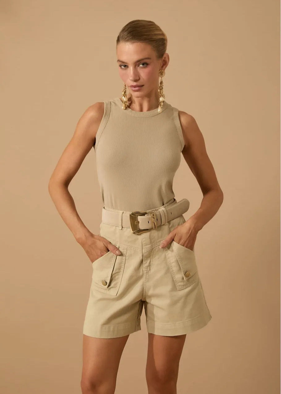 Woman wearing a beige sleeveless top and shorts with a belt against a beige background