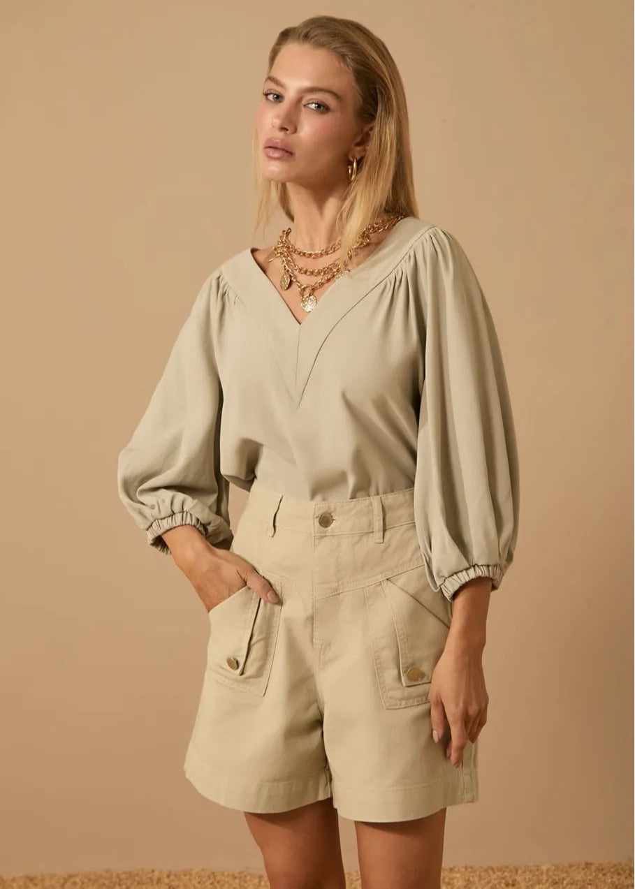 Woman wearing a beige blouse and shorts against a beige background
