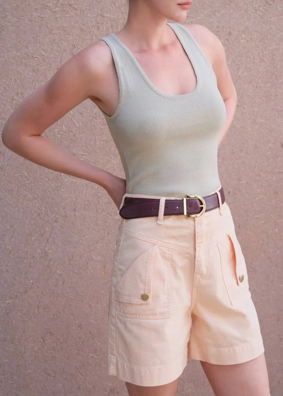 Person wearing a light green tank top and beige shorts against a plain background