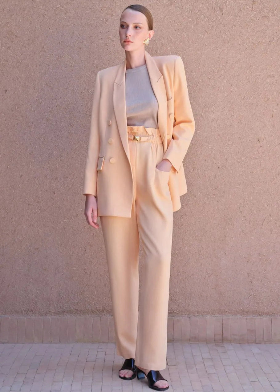 Woman wearing a peach suit standing against a beige wall.