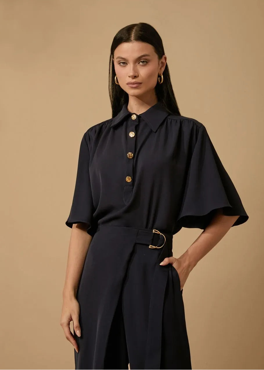 Woman wearing a dark blue outfit with gold buttons against a beige background