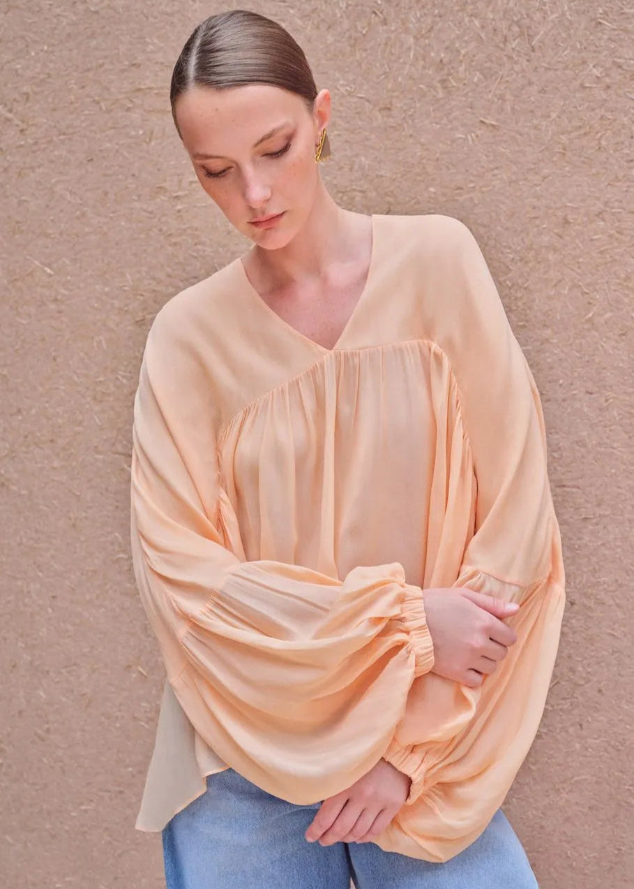 Woman wearing a light peach blouse against a beige background