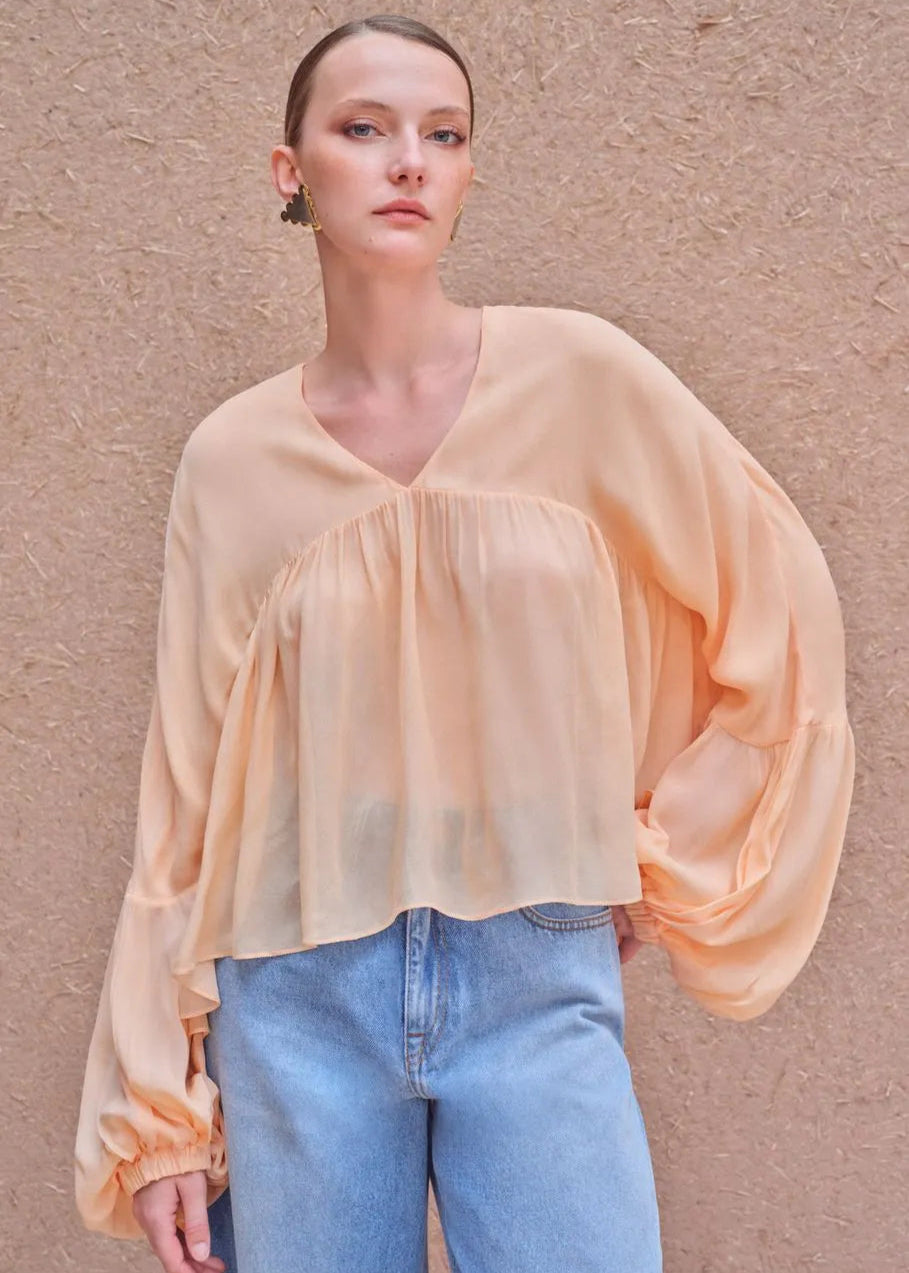 Woman wearing a sheer peach blouse and blue jeans against a beige background