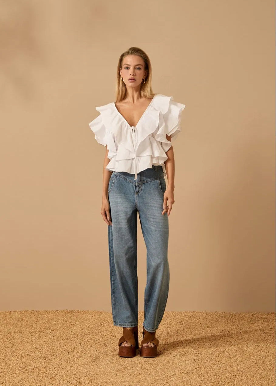 Woman wearing a white ruffled blouse and blue jeans against a beige background