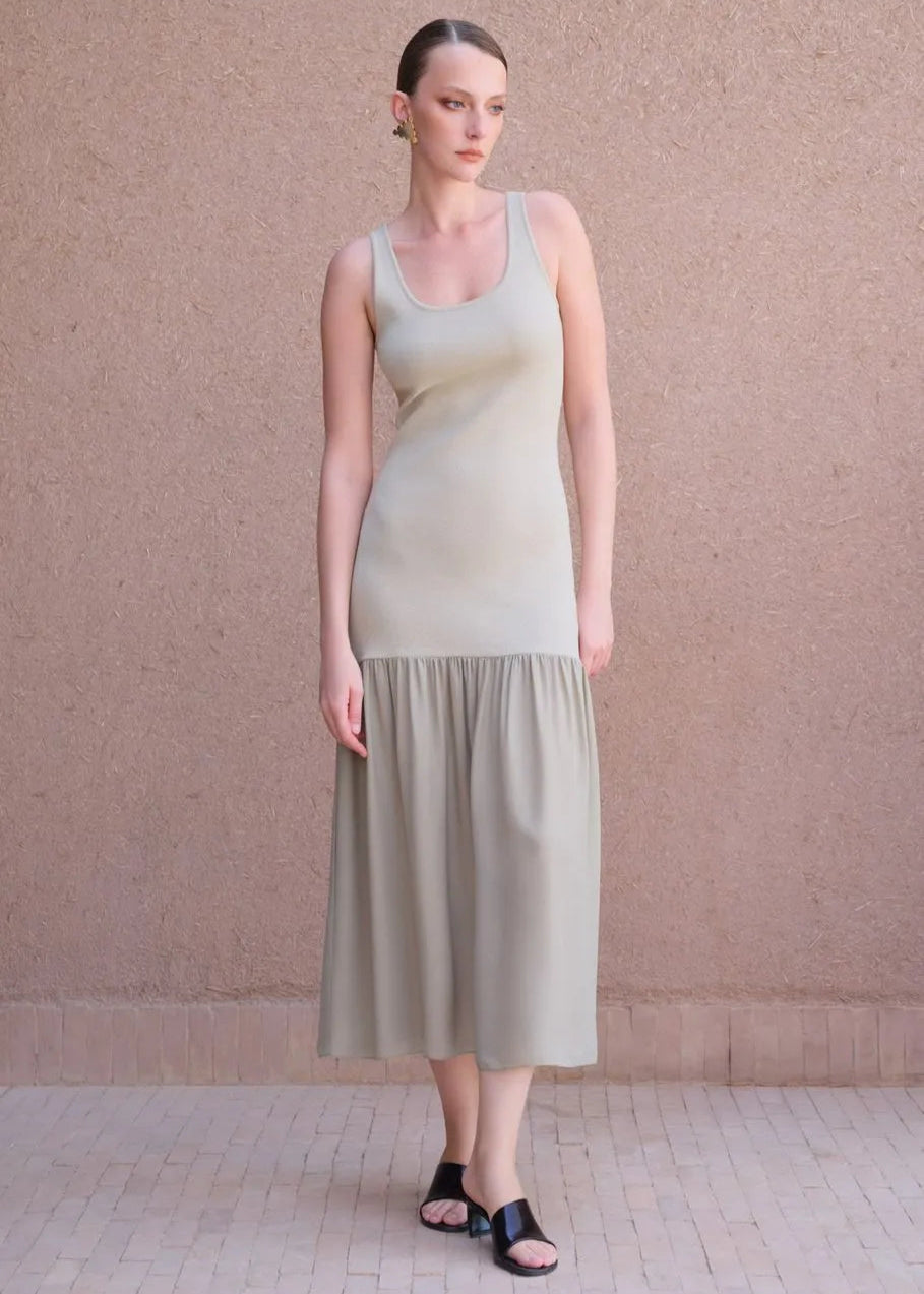 Woman wearing a light green dress standing against a beige wall.