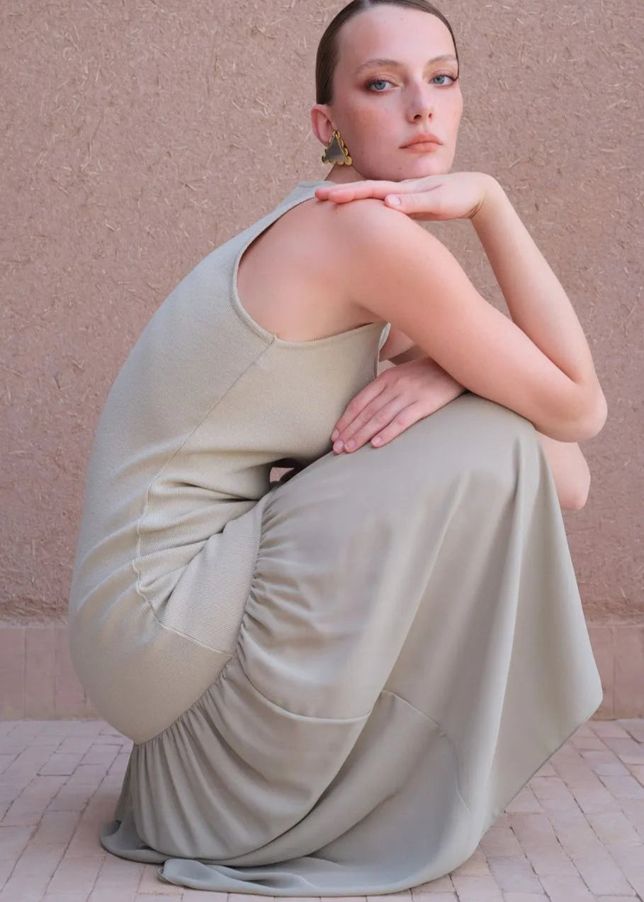 Woman in a flowing beige dress sitting against a pink wall.
