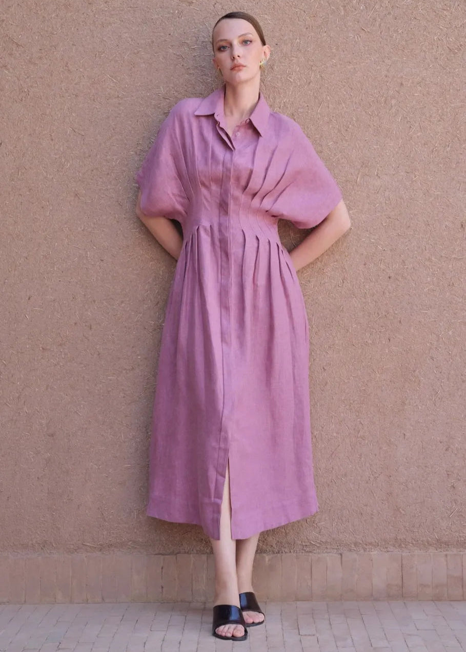 Woman wearing a pink dress standing against a beige wall.