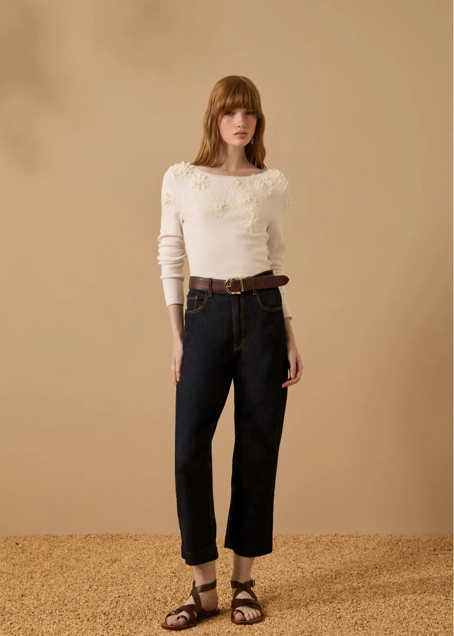 Woman wearing a white floral sweater and black jeans against a beige background