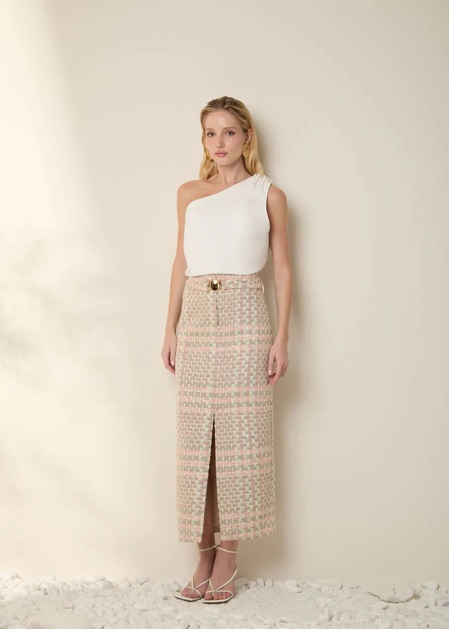 Woman wearing a white one-shoulder top and patterned skirt against a plain background