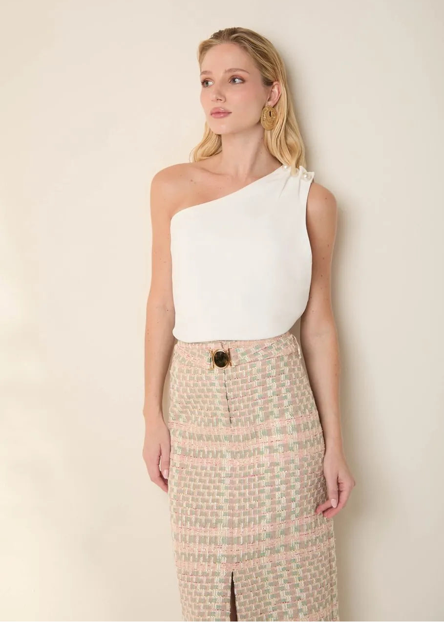 Woman wearing a white one-shoulder top and patterned skirt against a plain background
