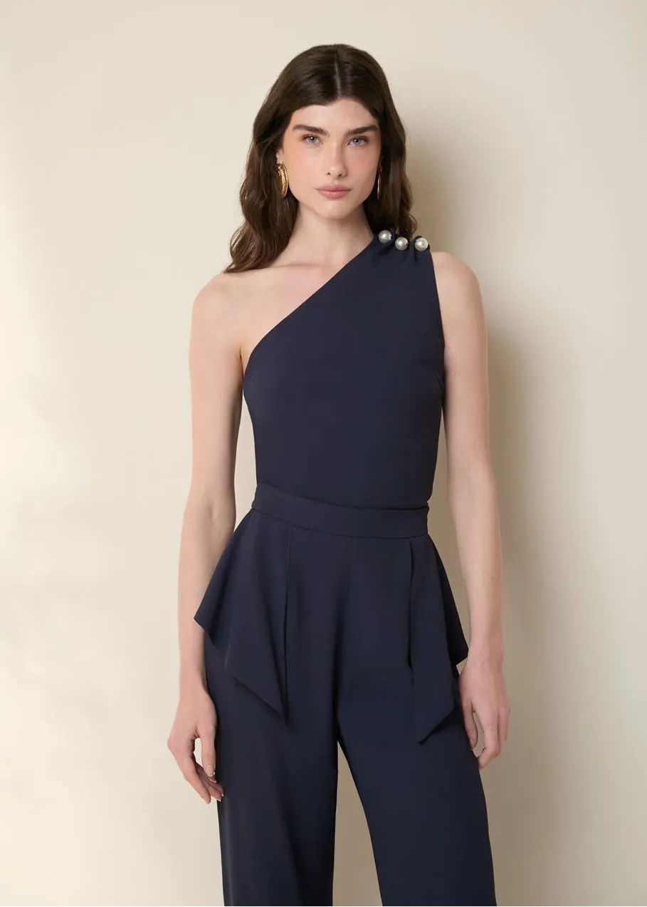 Woman wearing a navy one-shoulder jumpsuit against a beige background