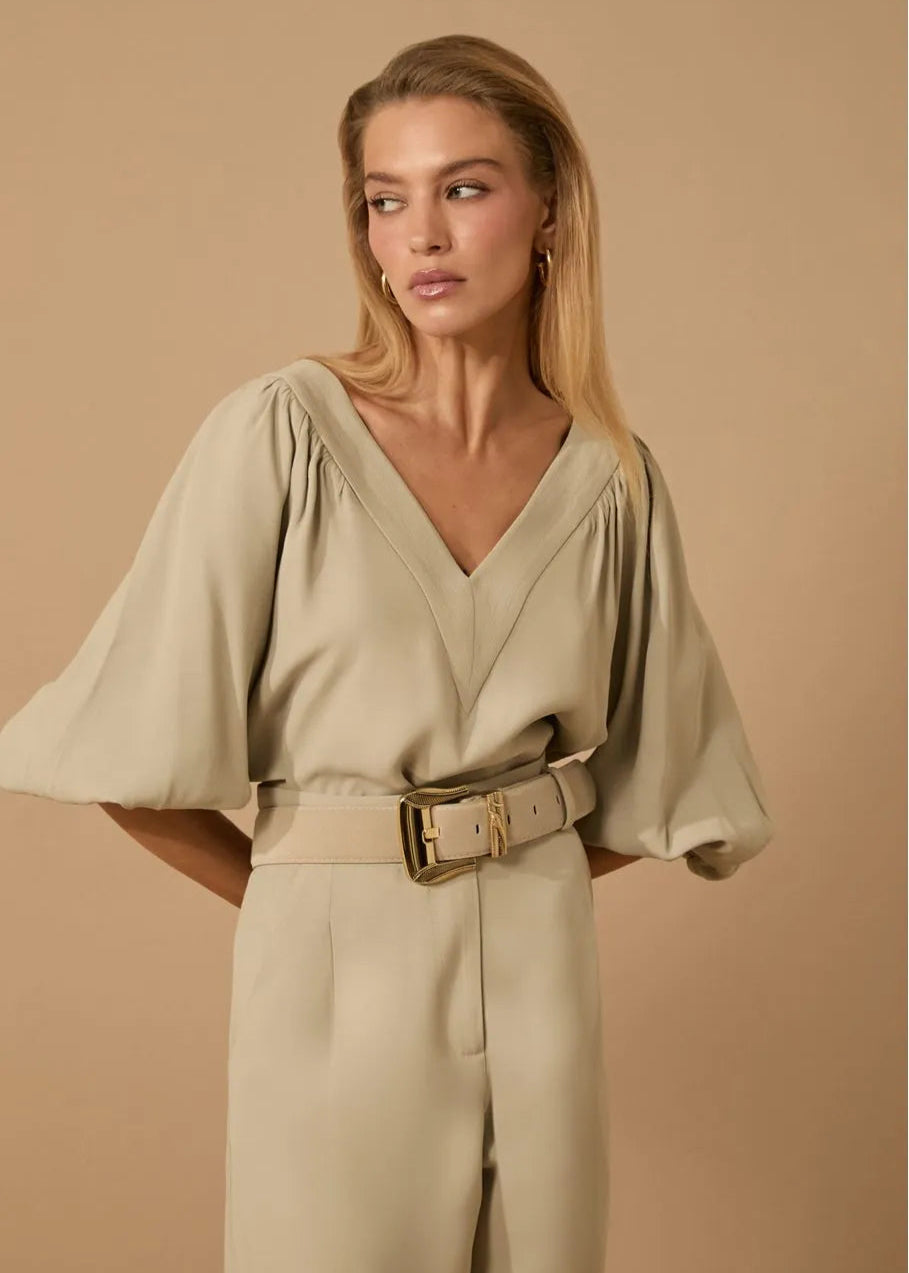 Woman wearing a beige outfit with a belt against a beige background