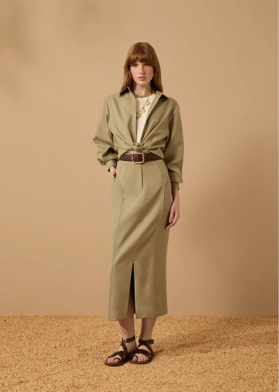 Woman wearing a green trench coat over a white shirt on a beige background
