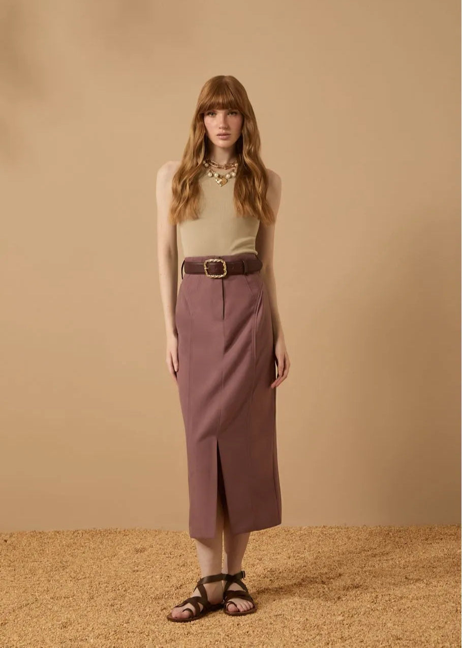 Woman wearing a beige top and purple skirt against a beige background