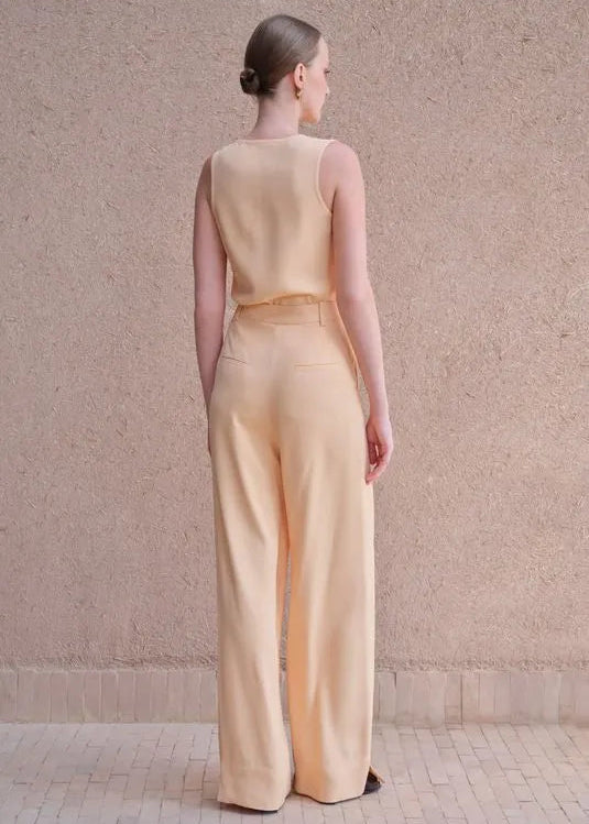 Woman wearing a beige outfit standing against a textured wall.