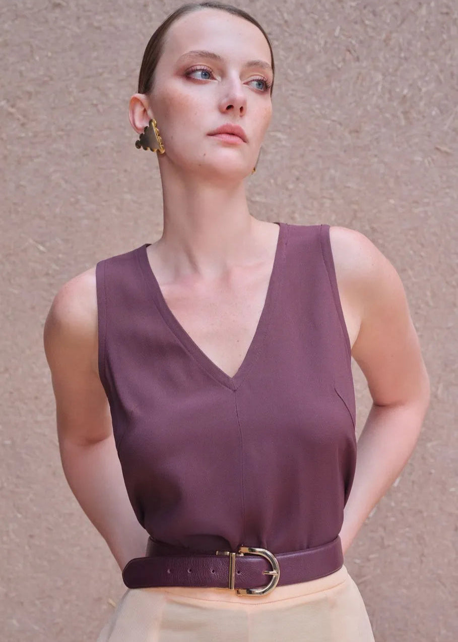 Woman wearing a purple sleeveless top with a belt against a beige background