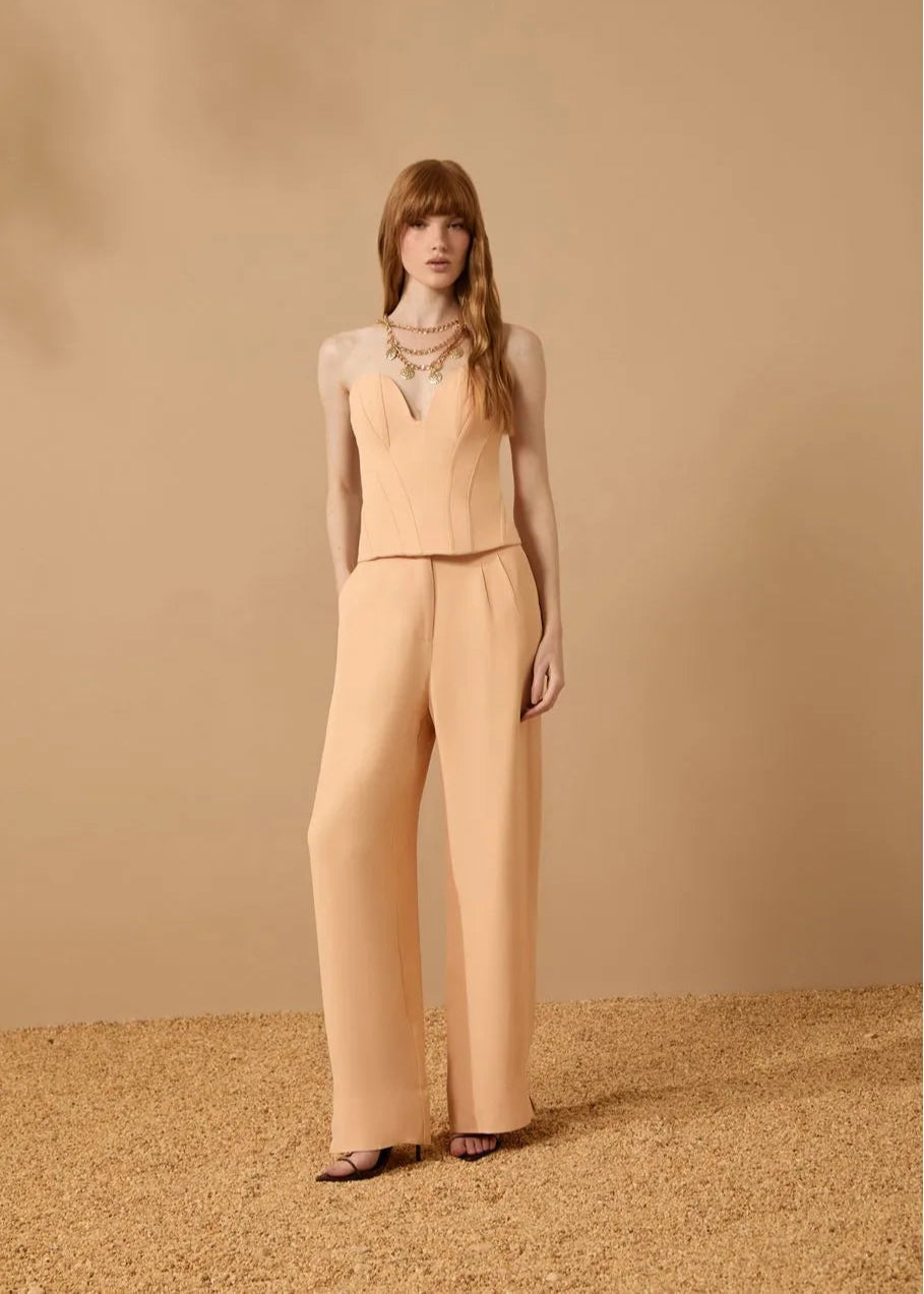 Woman wearing a beige sleeveless top and wide-leg pants against a beige background