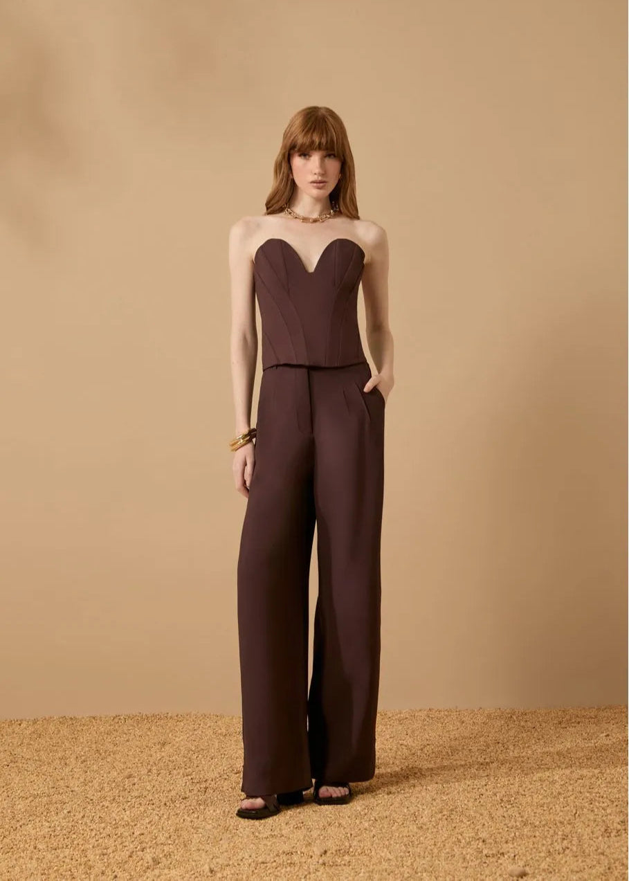Woman wearing a brown strapless top and wide-leg pants against a beige background