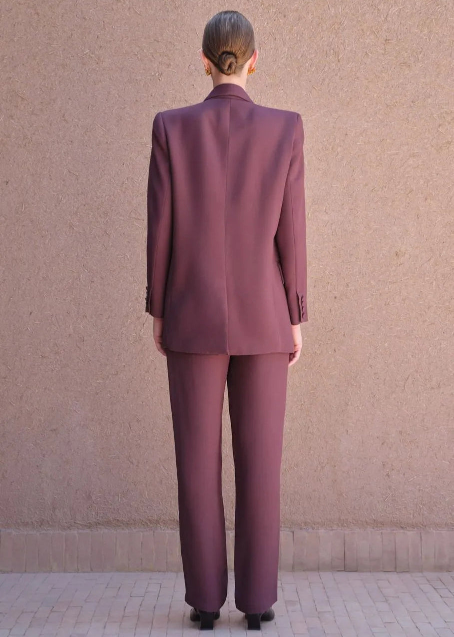Person wearing a maroon suit standing against a beige wall.