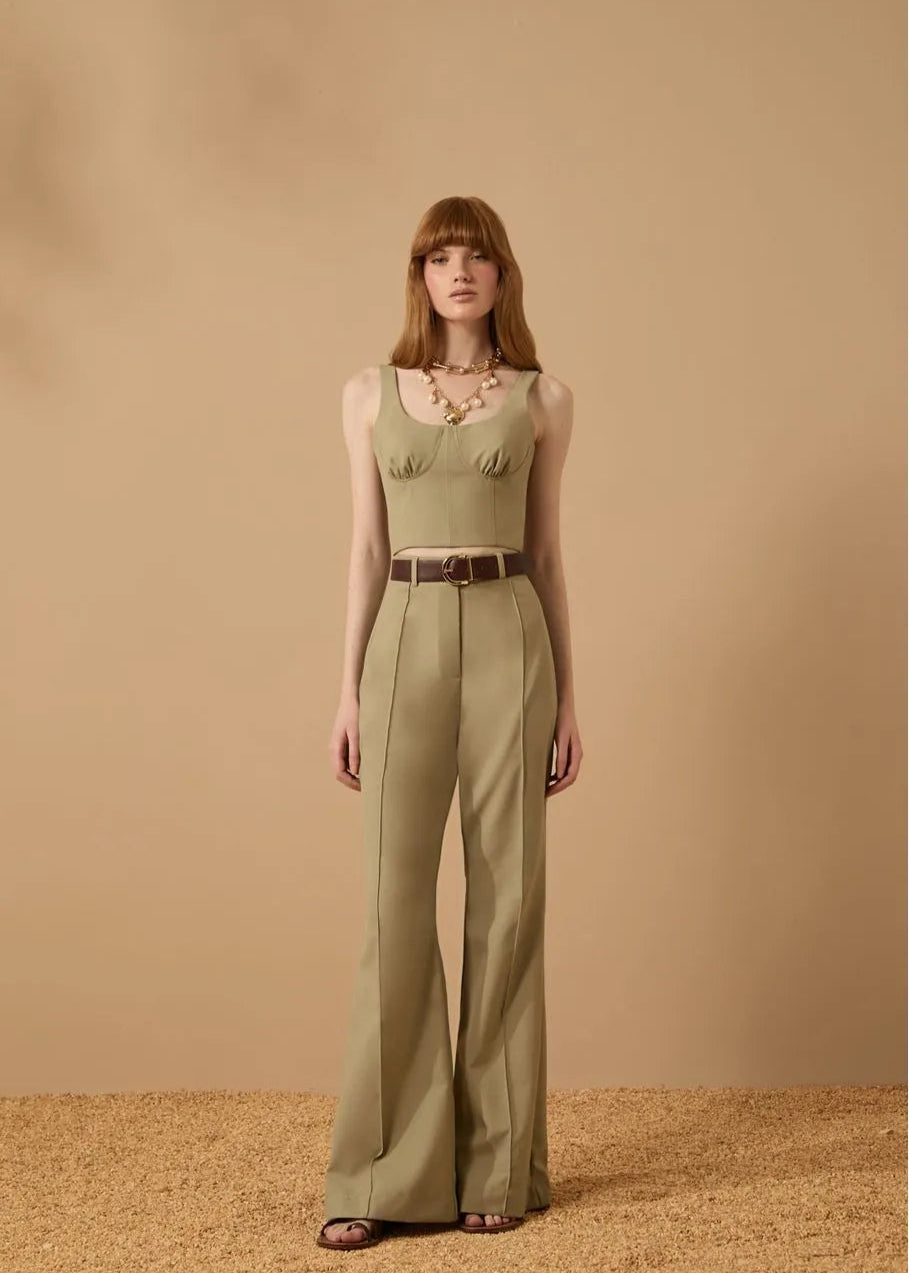 Woman wearing a green sleeveless top and high-waisted pants against a beige background