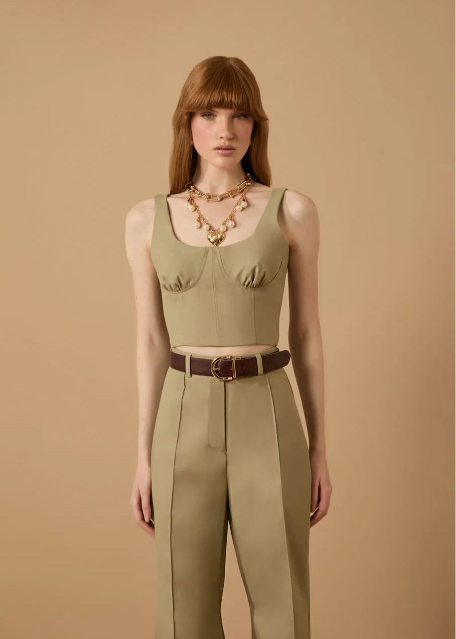 Woman wearing a green sleeveless top and beige pants against a beige background