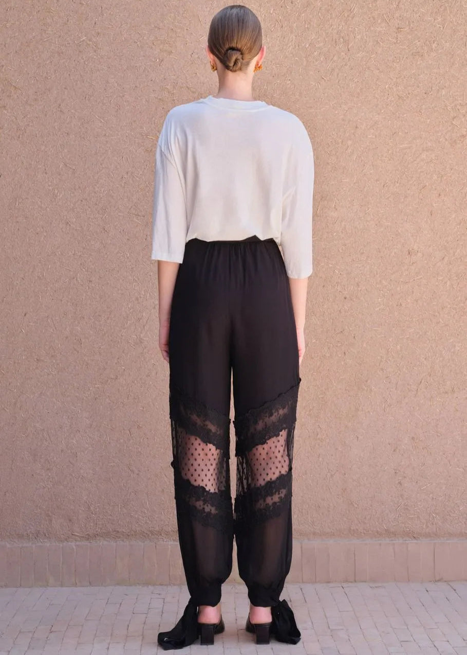 Person wearing a white top and black pants with lace details against a beige wall.