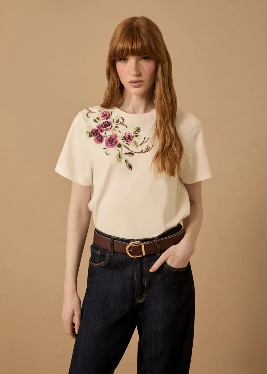 Woman wearing a white blouse with floral embroidery and dark jeans on a beige background