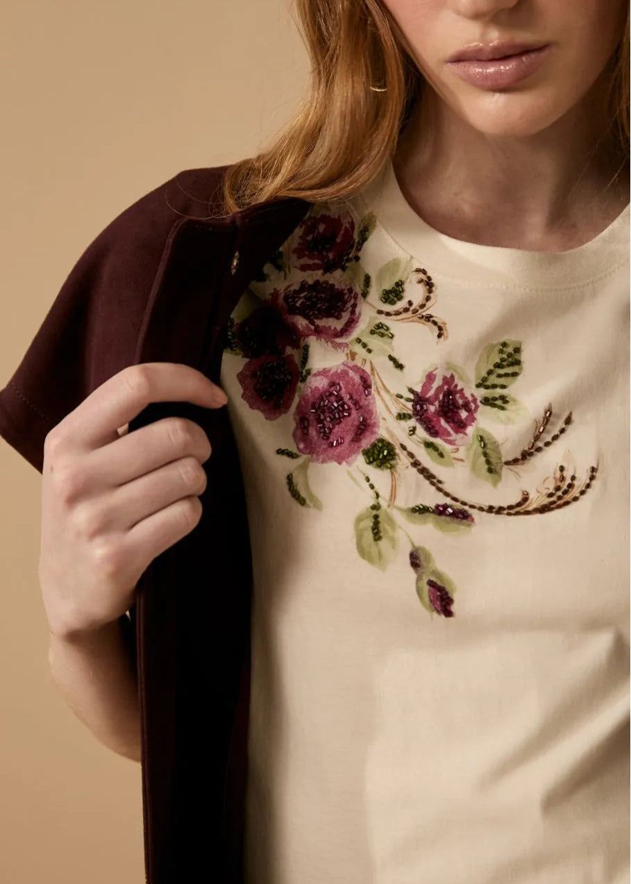 Person wearing a white shirt with floral embroidery on a beige background