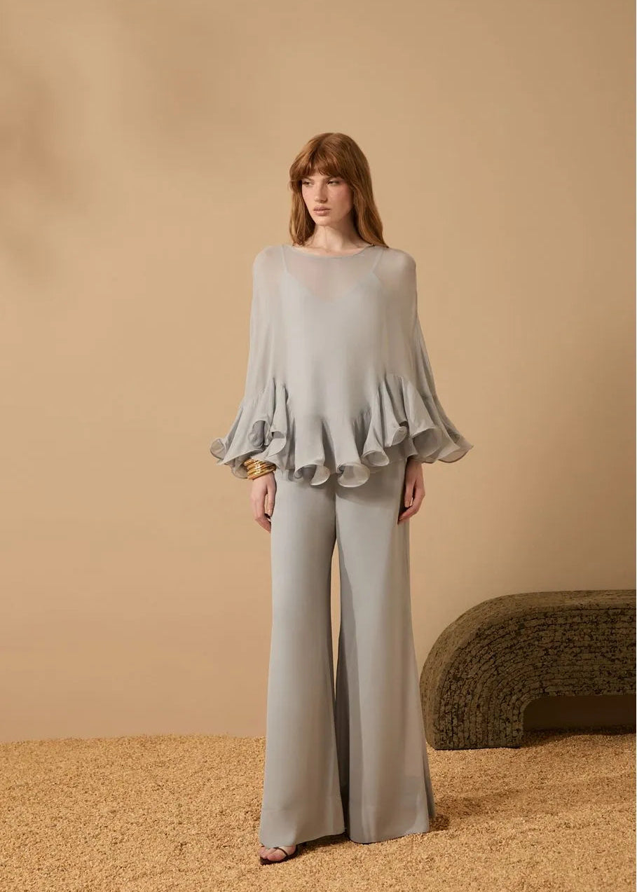 Woman wearing a light gray ruffled blouse and wide-leg pants against a beige background