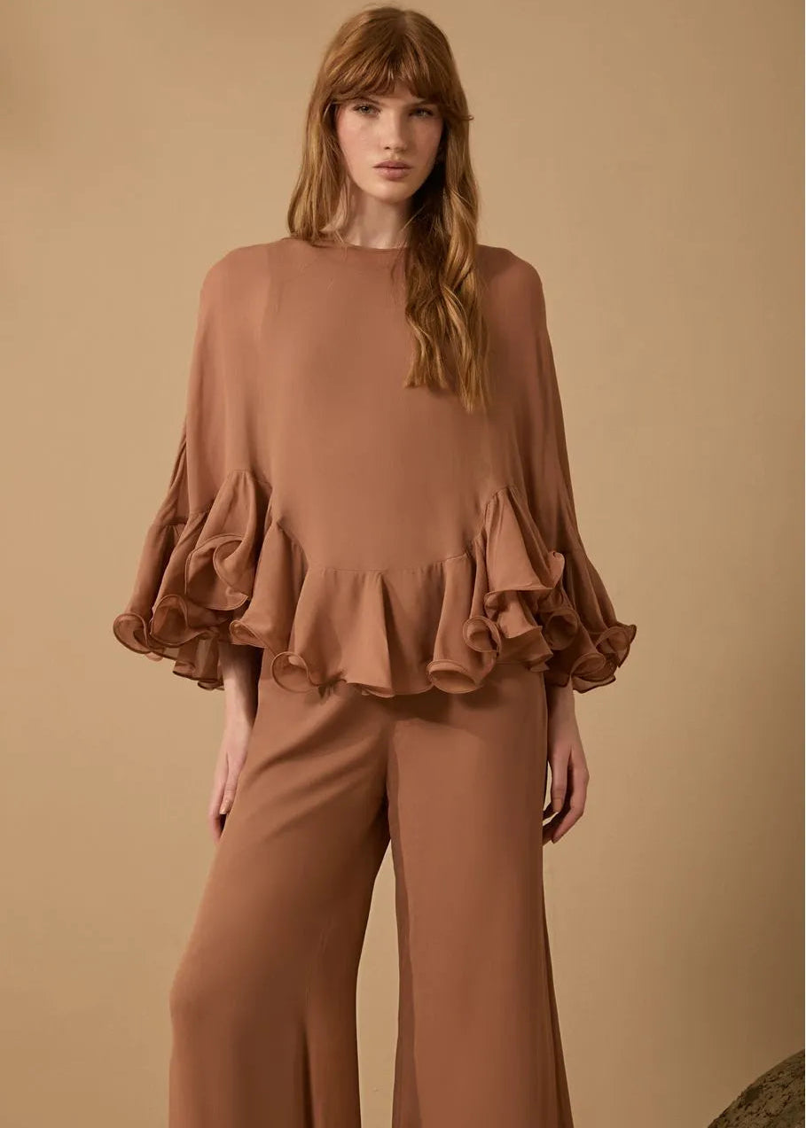 Woman wearing a brown ruffled top and pants against a beige background