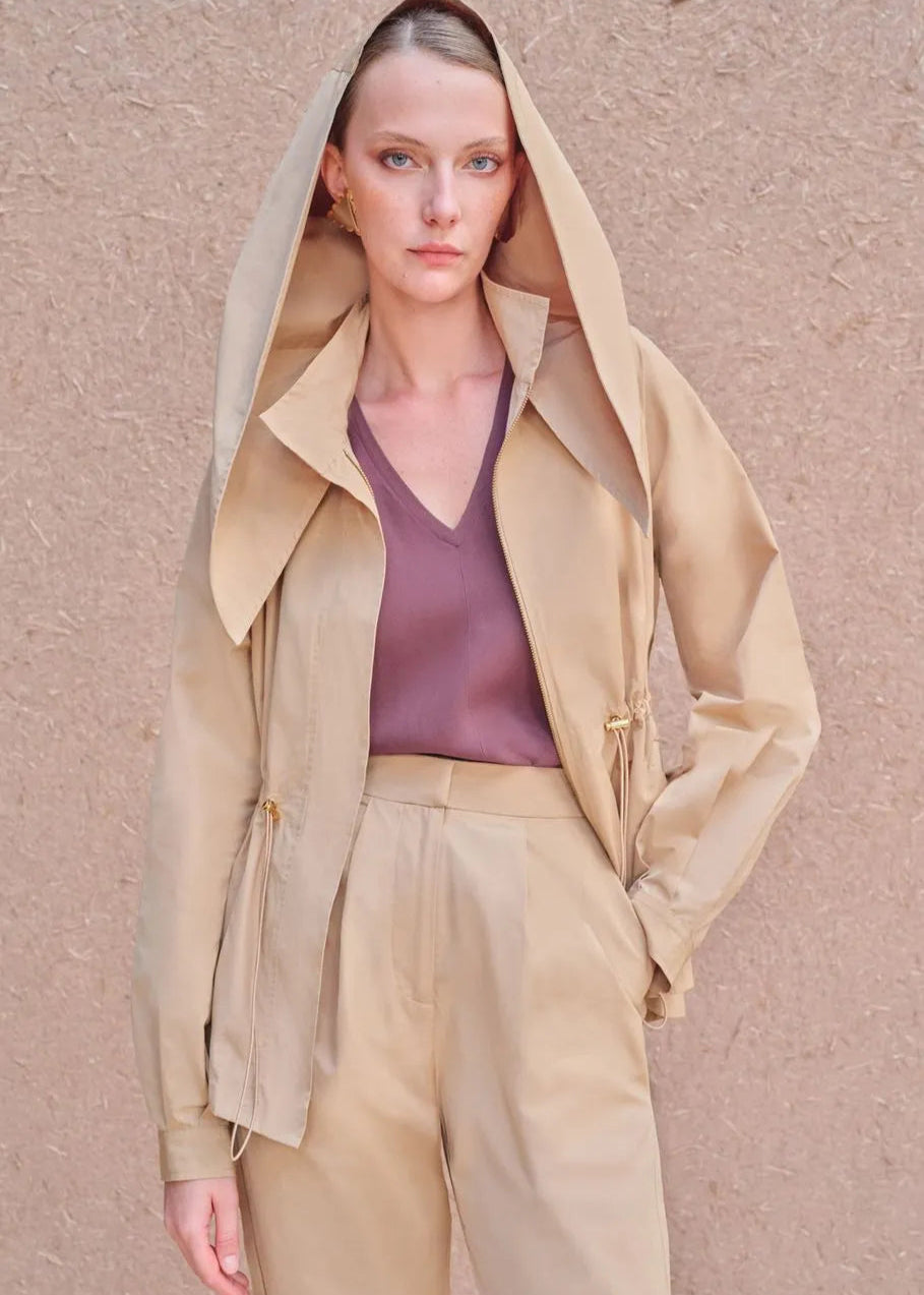 Woman wearing a beige trench coat over a pink top against a beige background