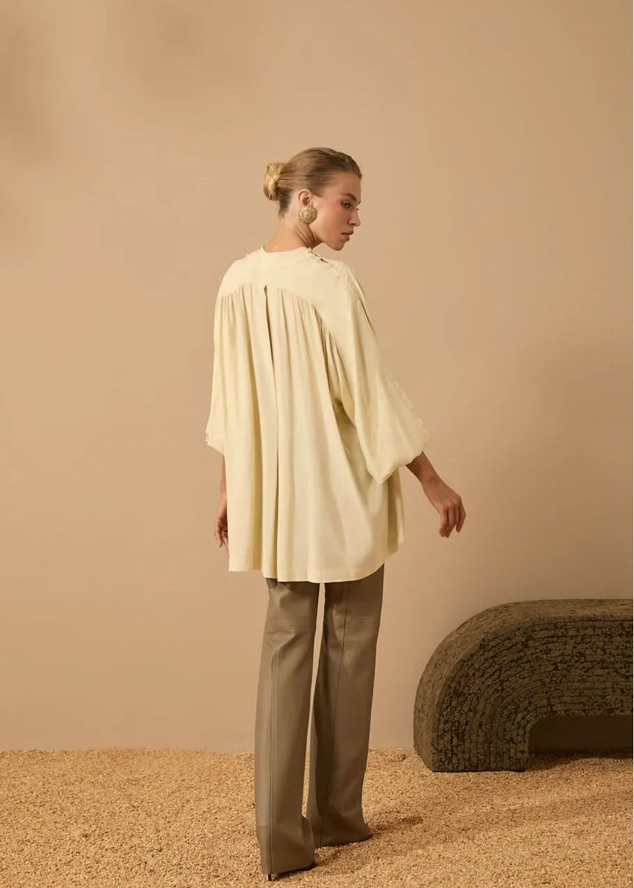 Woman wearing a light-colored top and beige pants against a beige background