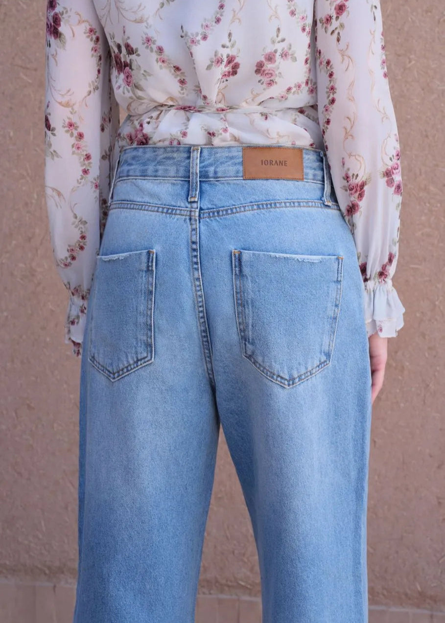 Person wearing light blue jeans with a floral blouse against a beige background