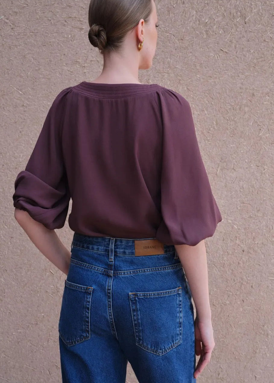 Person wearing a burgundy blouse and blue jeans against a beige wall