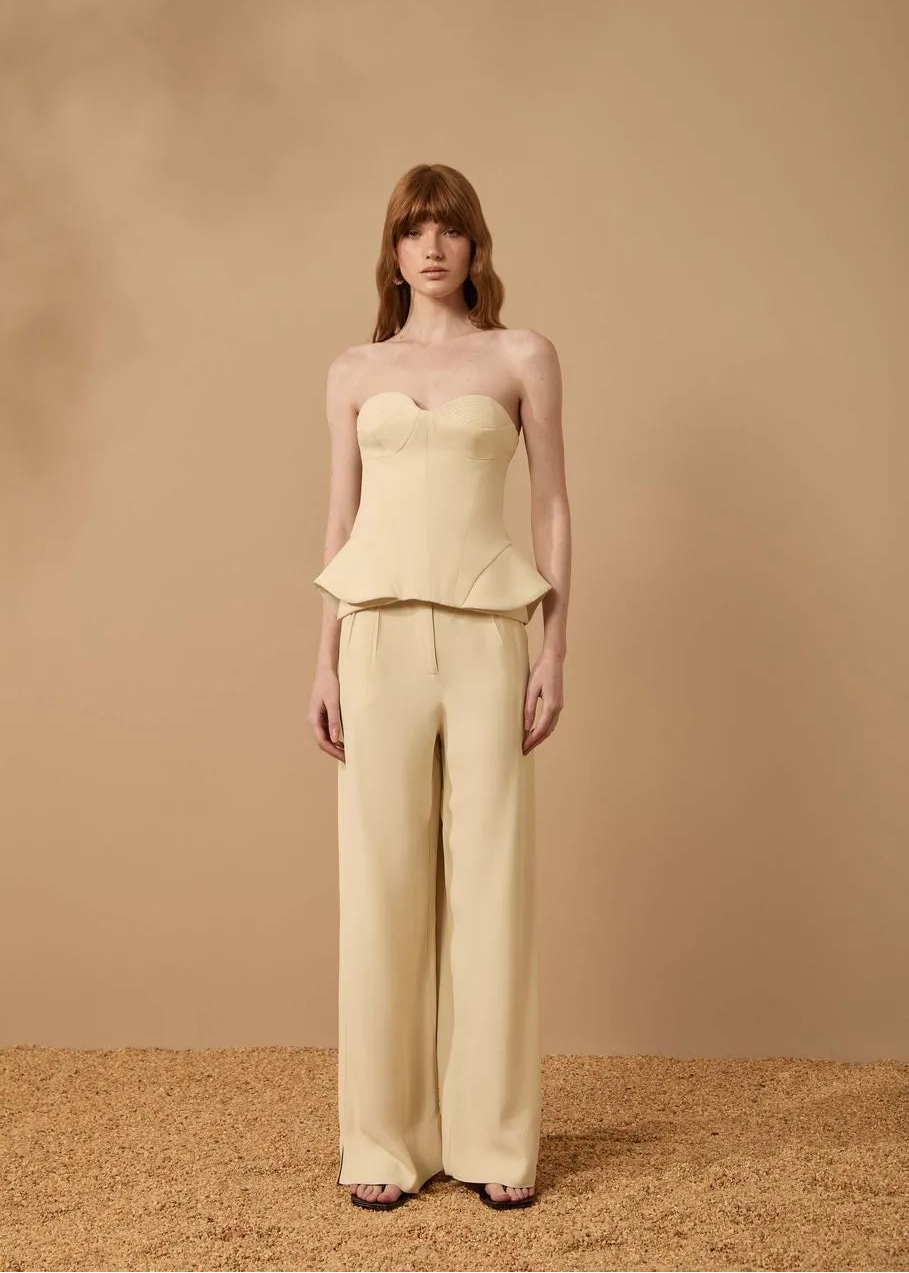 Woman wearing a light yellow strapless top and wide-leg pants against a beige background