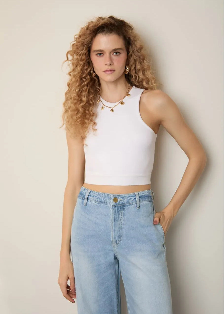 Woman wearing a white sleeveless top and light blue jeans against a plain background