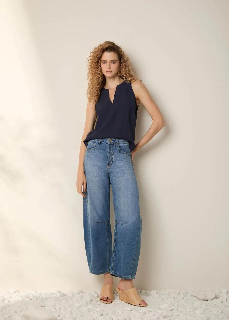 Woman wearing a navy sleeveless top and light blue jeans against a neutral background