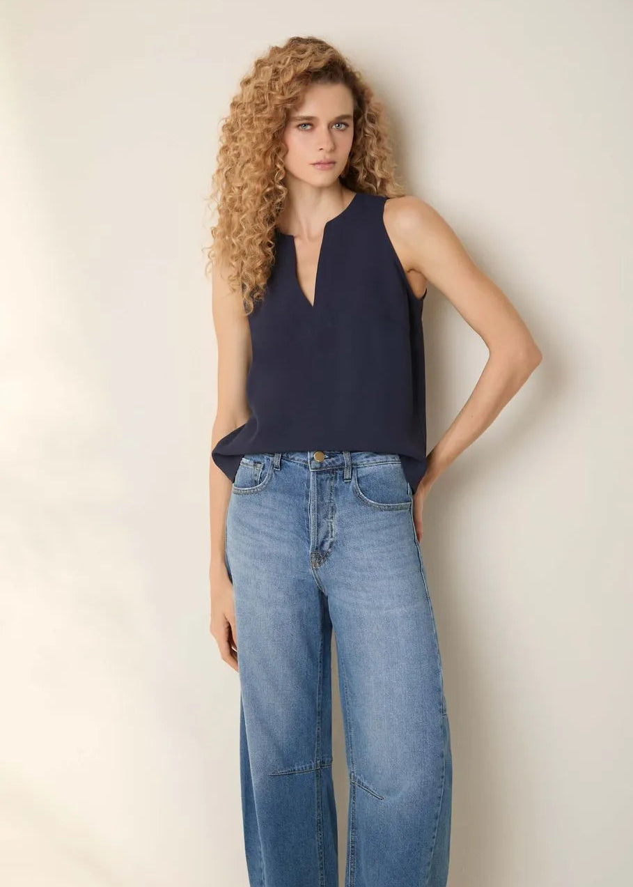 Woman wearing a navy sleeveless top and blue jeans against a plain background
