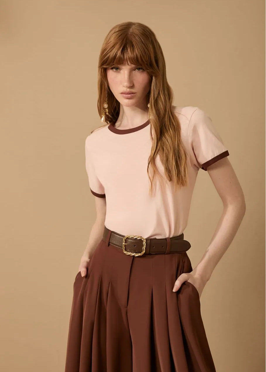 Woman wearing a light pink blouse with brown trim and a brown skirt on a beige background