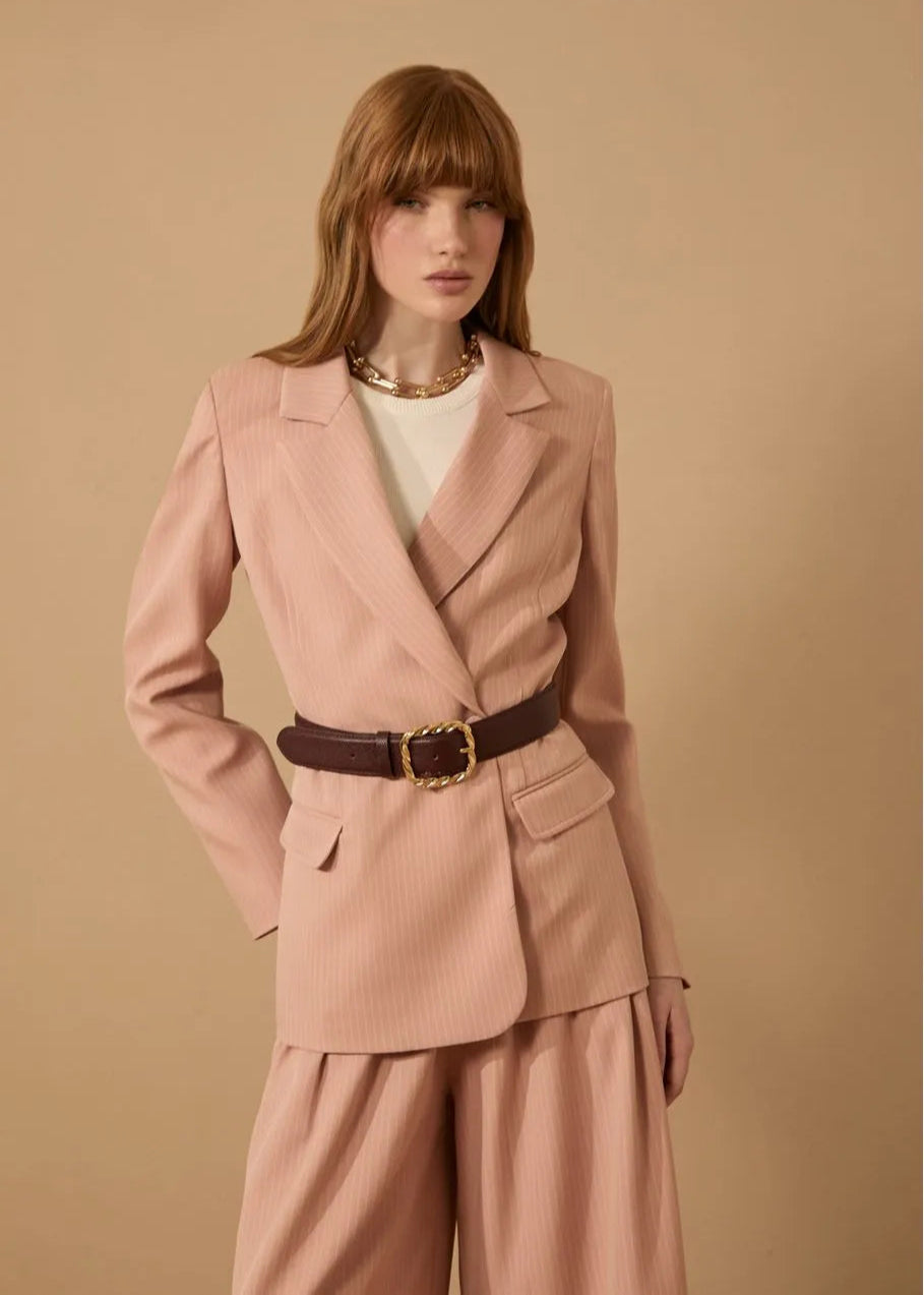 Woman wearing a pink suit with a brown belt against a beige background