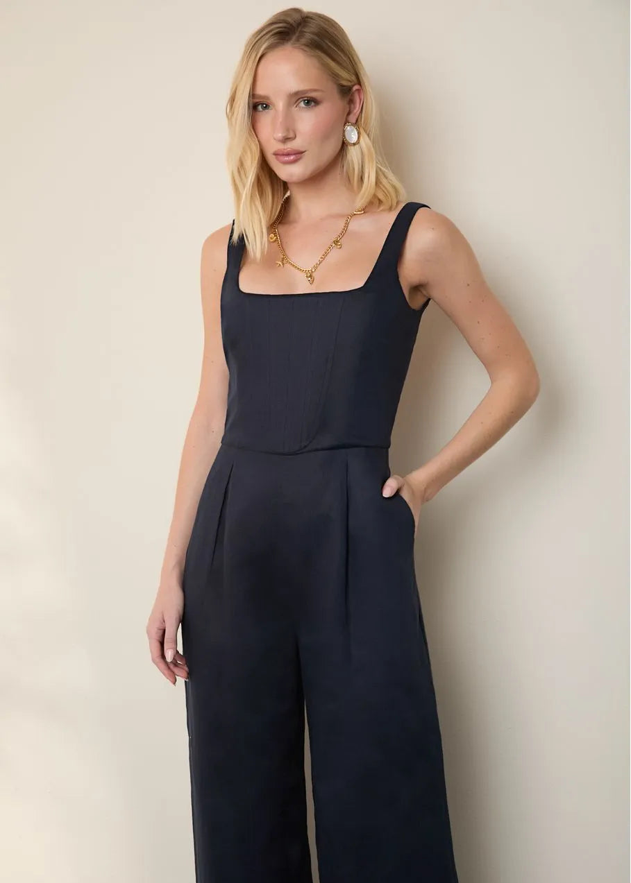 Woman wearing a navy blue jumpsuit against a plain background