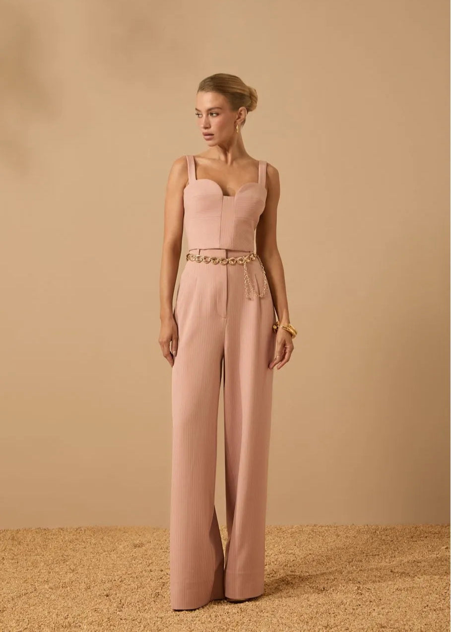 Woman wearing a pink jumpsuit with a gold belt against a beige background