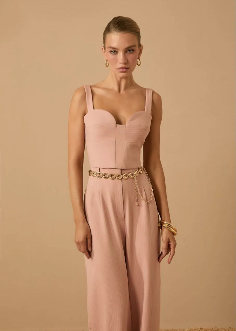 Woman wearing a pink jumpsuit with gold accents against a beige background