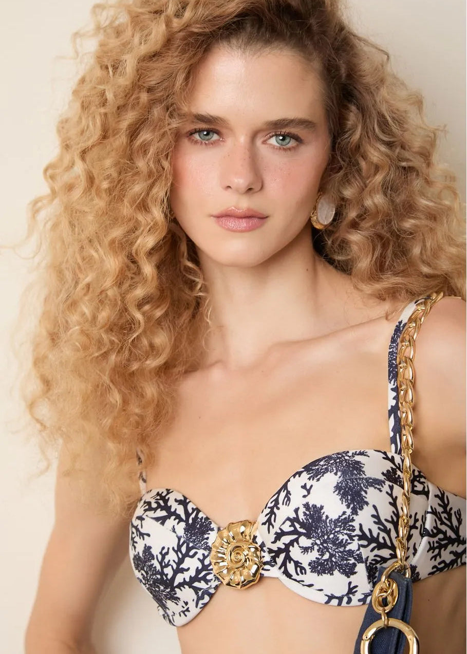 Woman wearing a patterned bikini top with gold accents against a neutral background