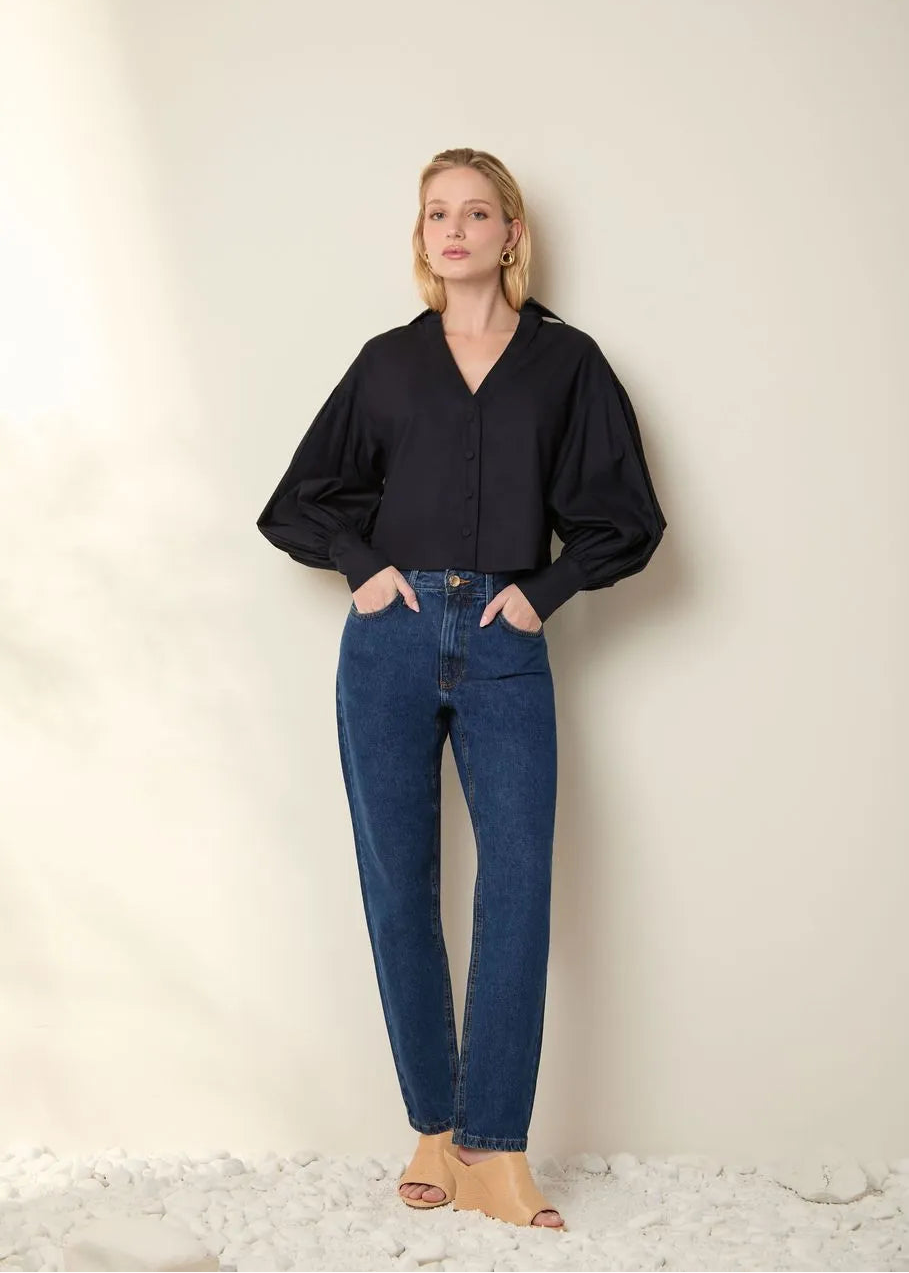 Woman wearing a black blouse and blue jeans against a plain background