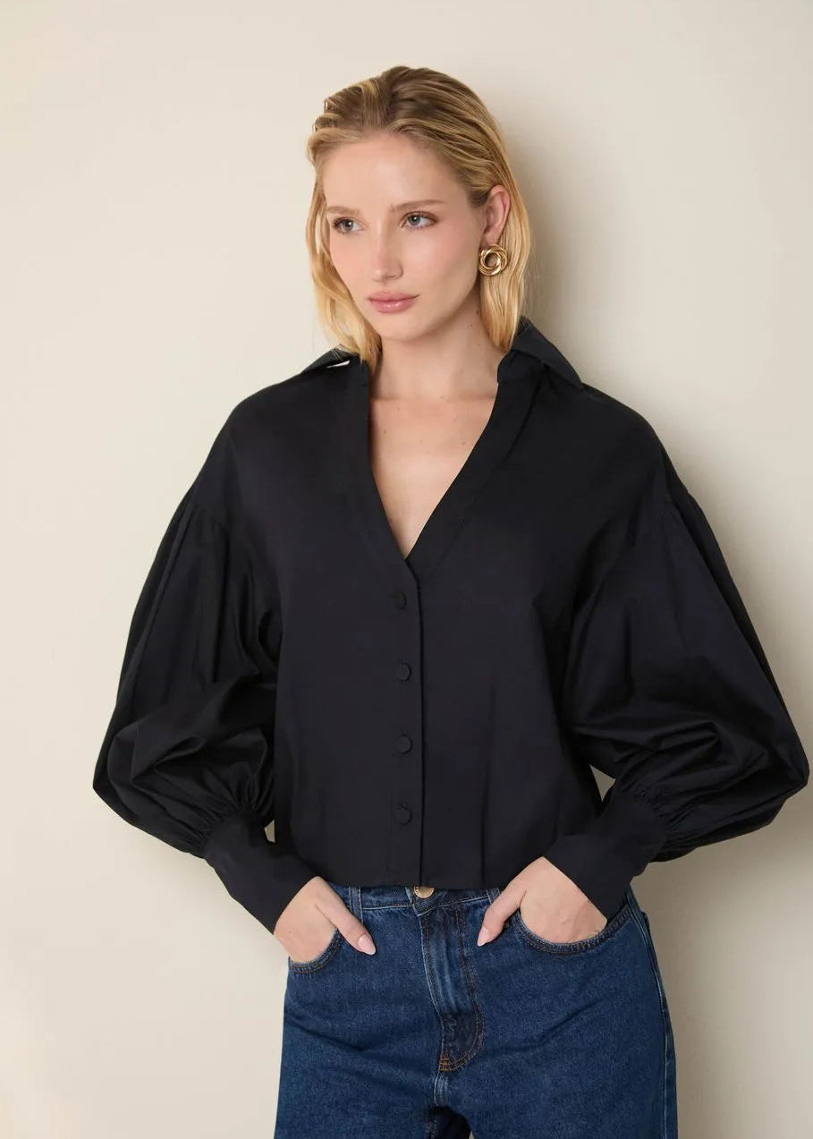 Woman wearing a black blouse and blue jeans against a beige background