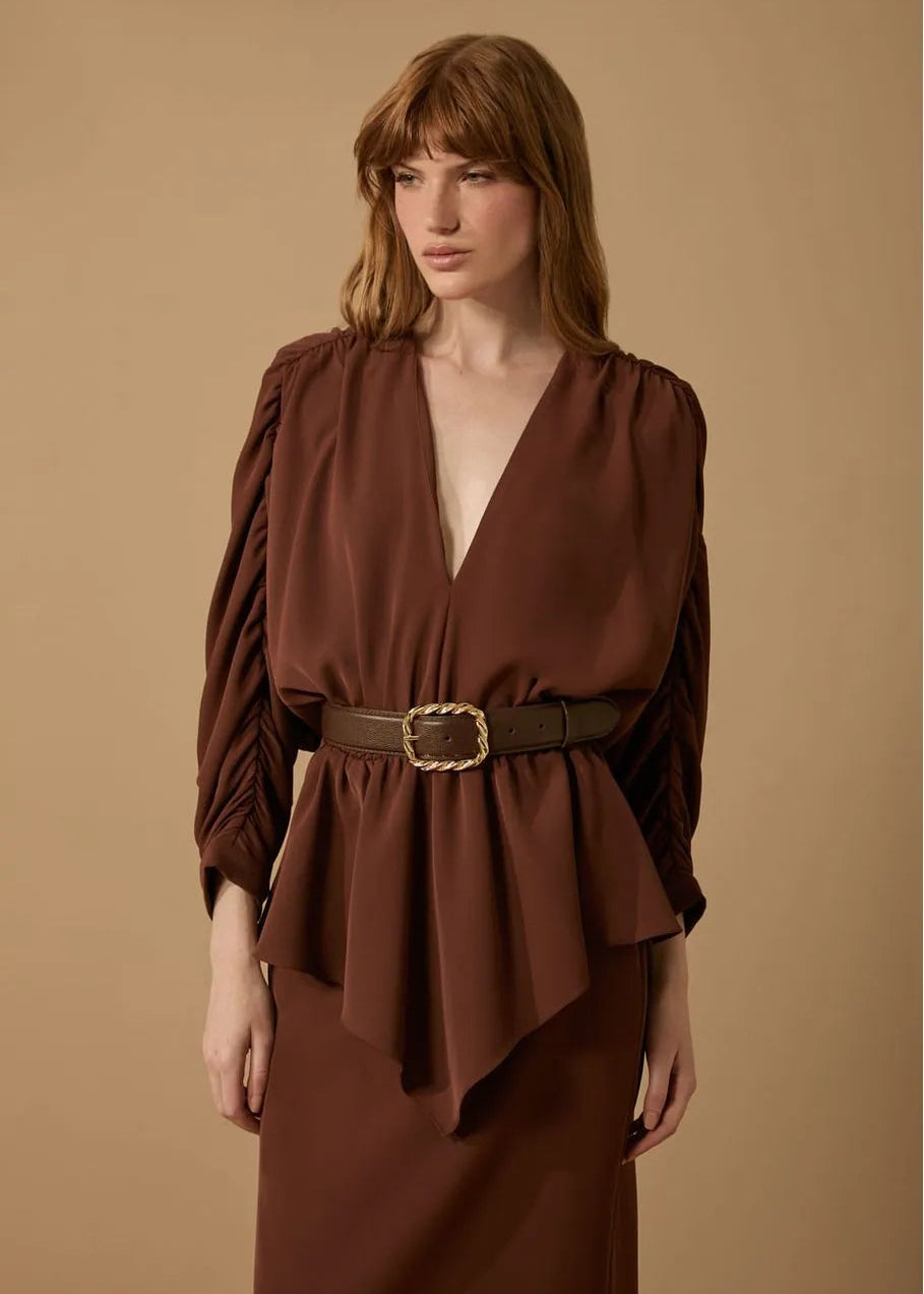 Woman wearing a brown dress with a belt against a beige background